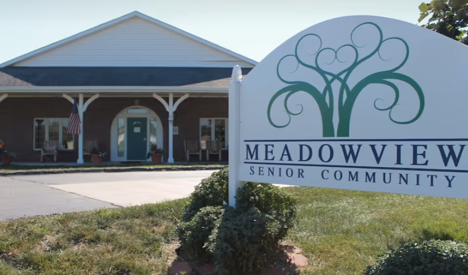 Front entrance of a brick senior living building with a large 'Meadowview Senior Community' sign in the foreground.