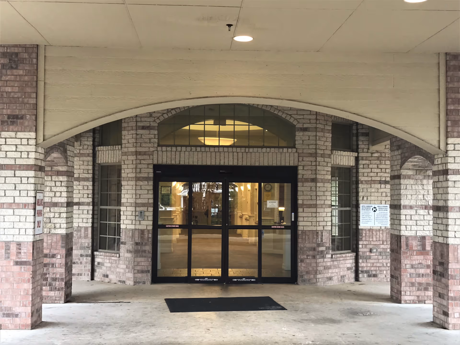 Arched covered entrance to a brick health center building with glass double doors and a floor mat.