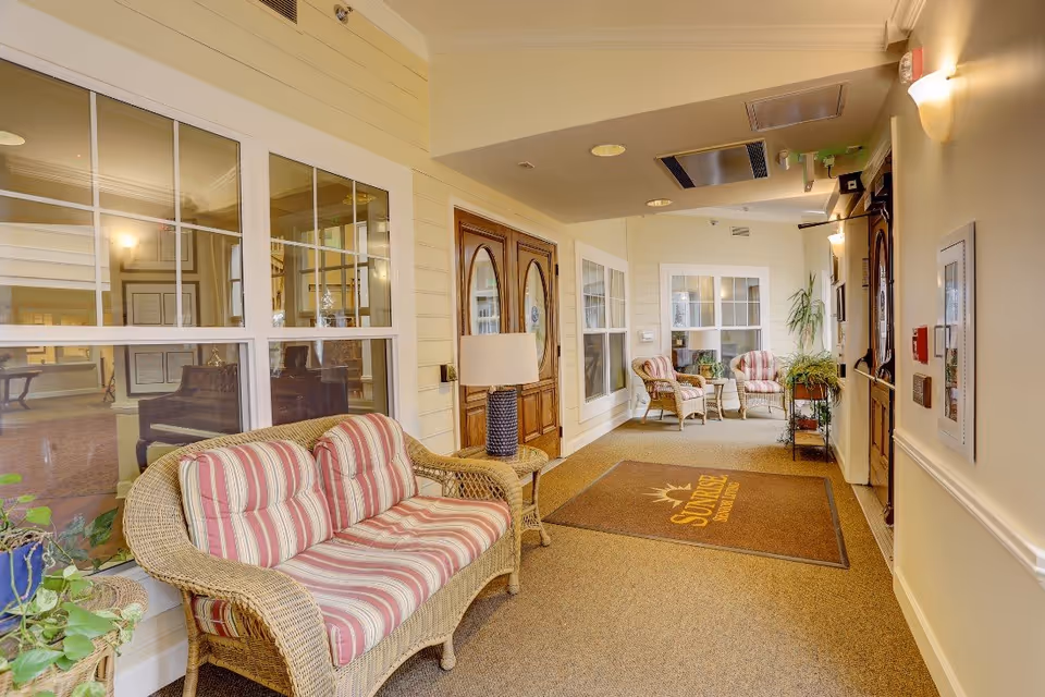 Carpeted entry corridor with wicker sofas and chairs, striped cushions, plants, lamps and a 'Sunrise' welcome mat.