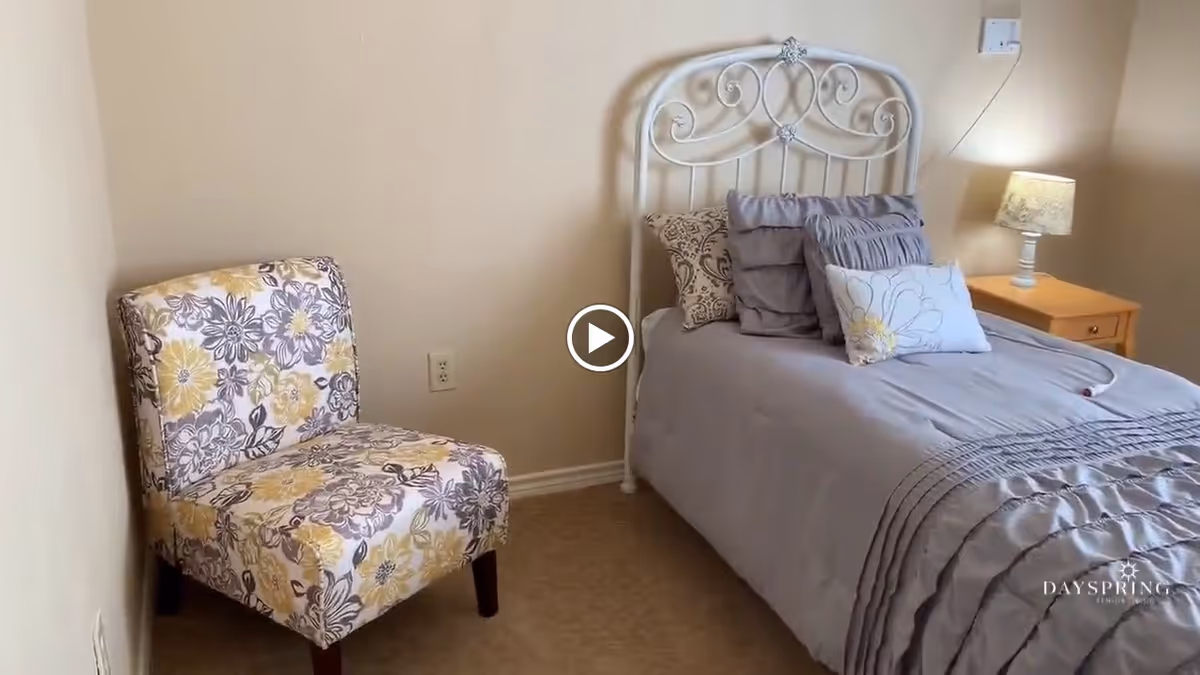 Small bedroom with a white decorative metal headboard bed, gray bedding, a floral accent chair, and a nightstand with a lamp.