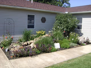 Exterior view of a single story assisted living building with a well-kept garden along a walkway.