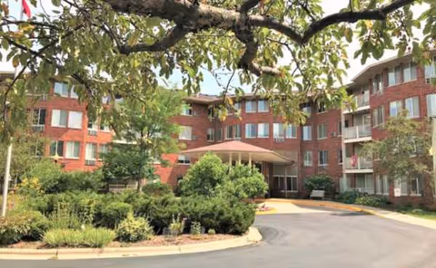 Brick senior living building with circular driveway, entrance canopy, and landscaped courtyard.