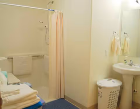 Small bathroom with shower curtain, sink, mirror, towels, and a laundry hamper.
