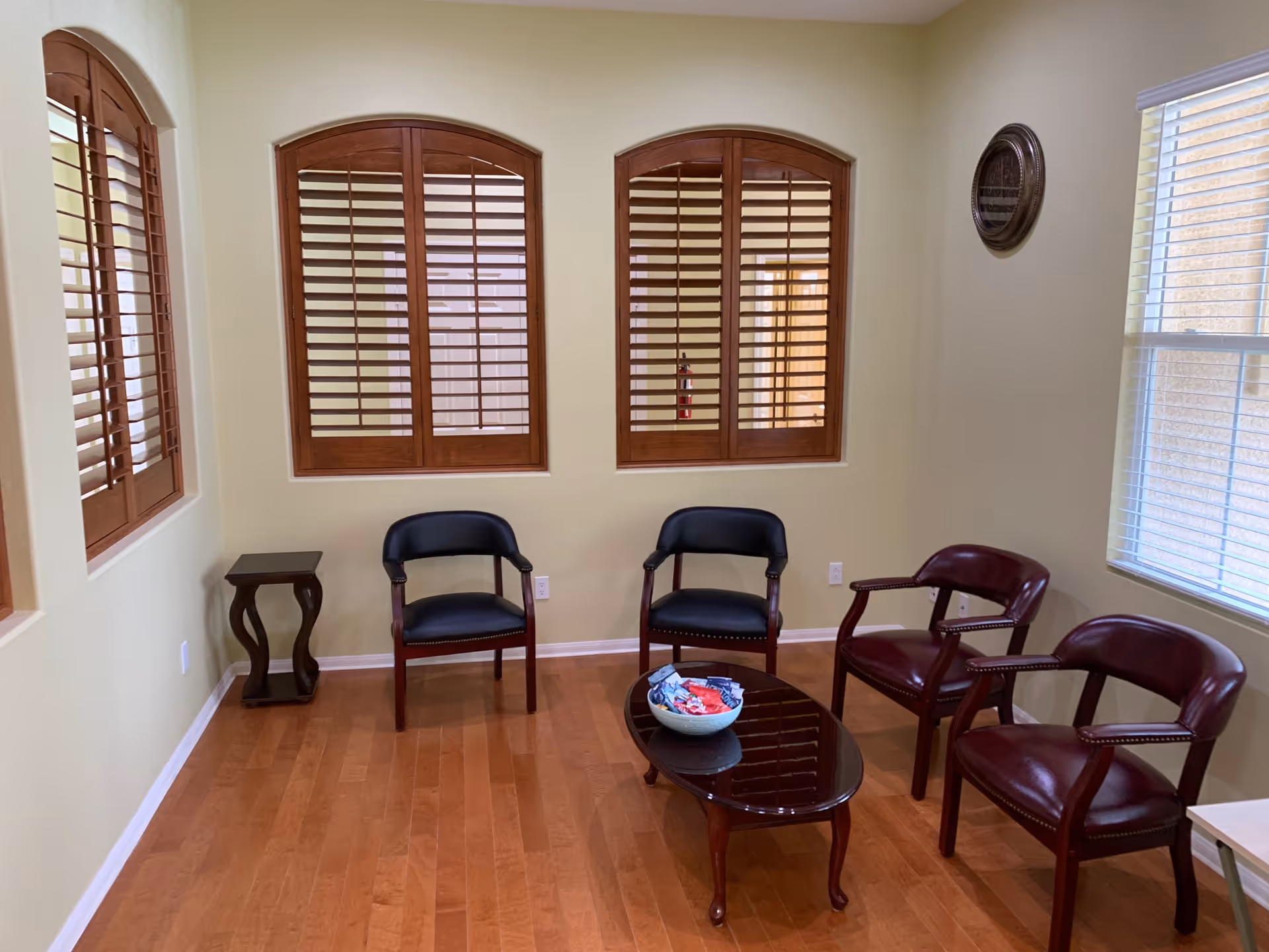 Small seating area with four chairs around a wooden coffee table, hardwood floors, and shuttered windows.