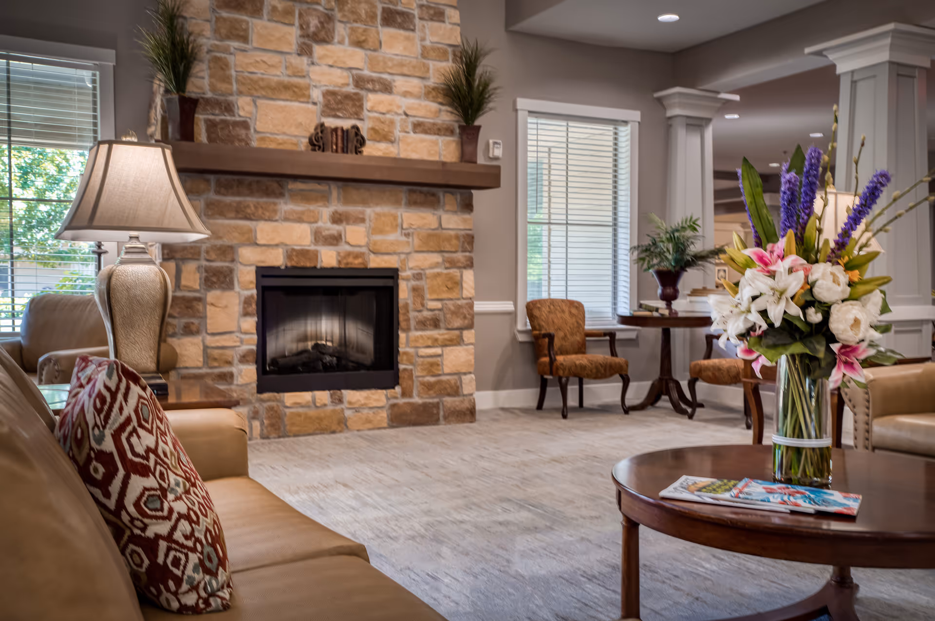 Furnished common living room with a stone fireplace, sofa and chairs, and a coffee table holding a vase of flowers and magazines.