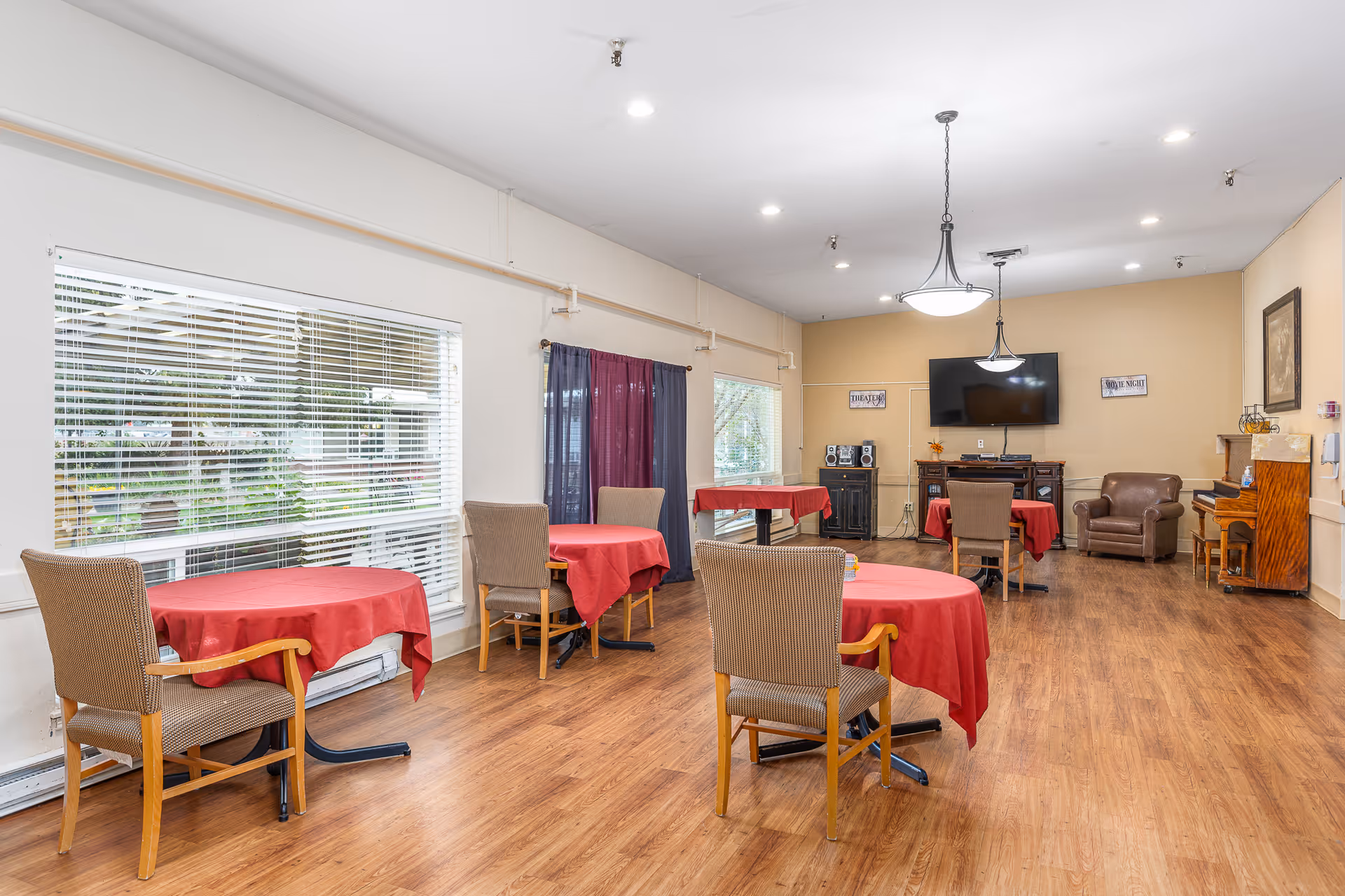 A cozy dining area with red tablecloths and a television in a senior living facility.