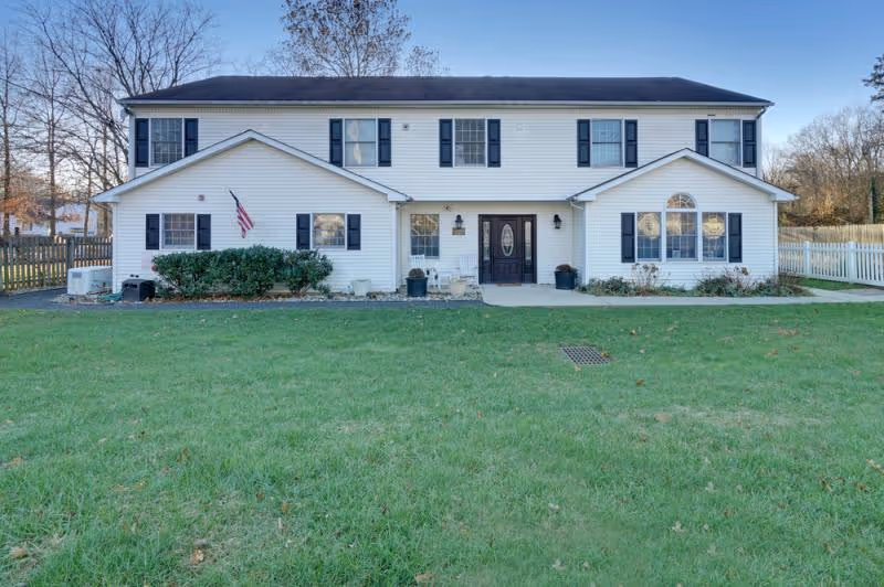 Two-story white facility with black shutters, central entrance, and a green front lawn.