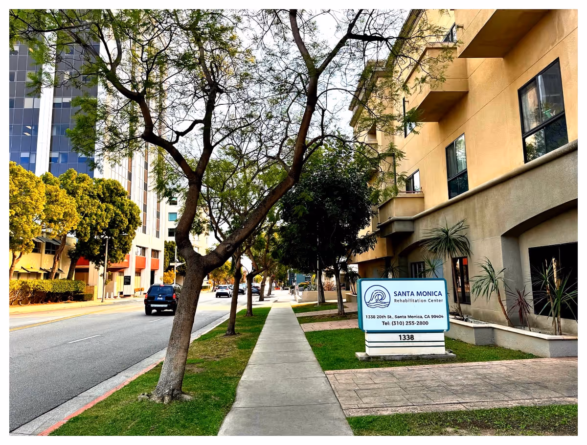 Sidewalk and street view of the Santa Monica Rehabilitation Center building and sign with trees lining the front.
