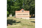 A brick and stone sign for Mcauley Residence situated on a grassy area with trees in the background.