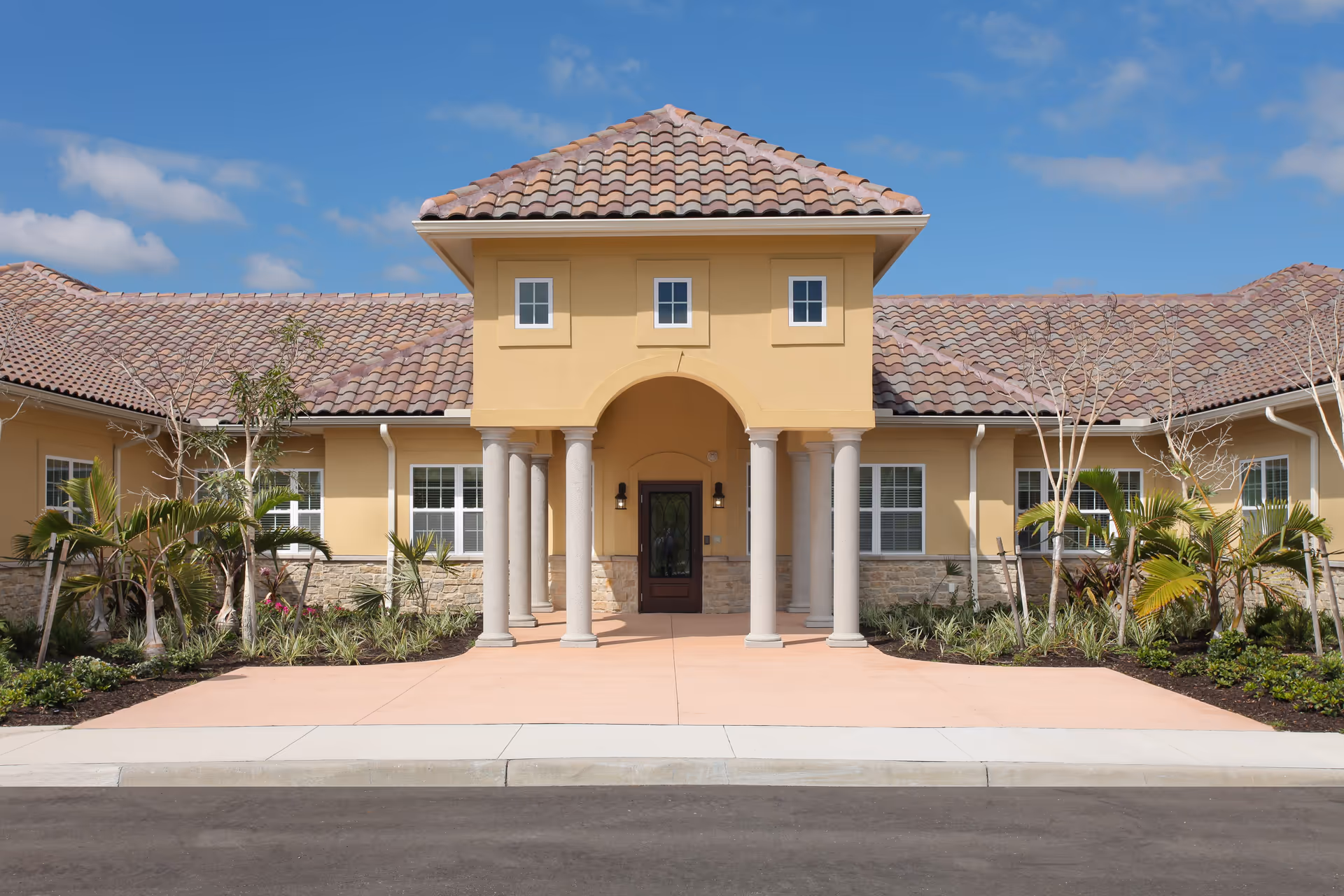 Front entrance of a Mediterranean-style building with columns, tiled roof, and landscaped grounds.