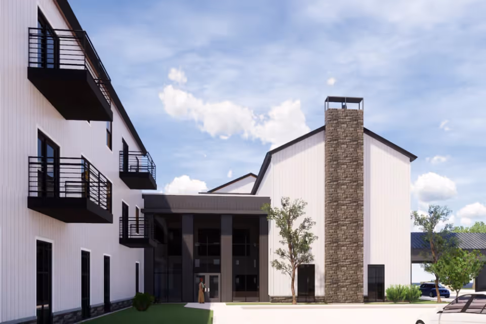 Exterior view of a modern senior living facility building with white siding, black balconies, large windows, and a stone chimney under a partly cloudy sky.