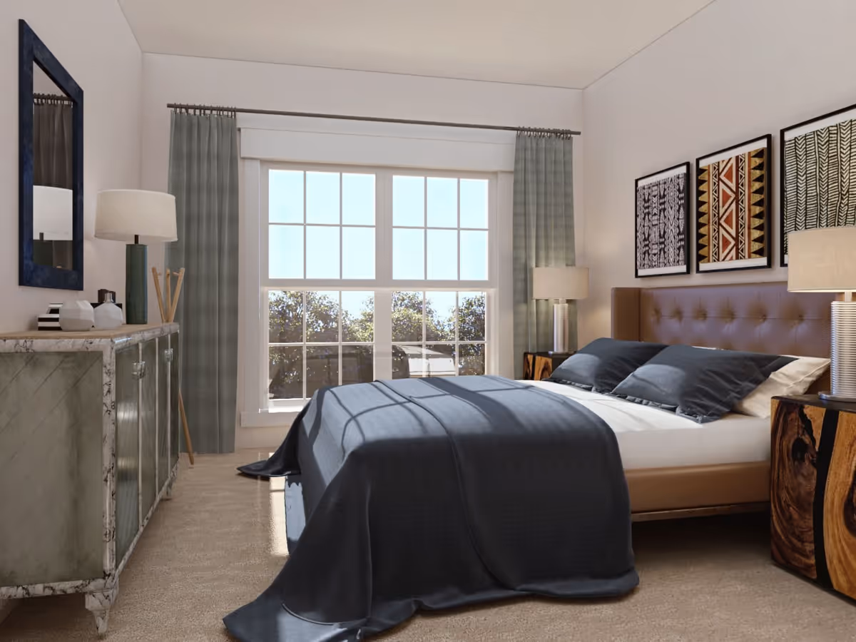 A bright bedroom with a large window letting in natural light. The room features a bed with a brown tufted headboard, dark gray bedding, and two wooden nightstands with lamps. On the left side, there is a marble-topped dresser with decorative items and a mirror above it. Light green curtains frame the window, and three framed abstract art pieces hang above the bed.