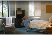 Furnished bedroom with a single bed, armchair, small dresser, and shuttered windows.