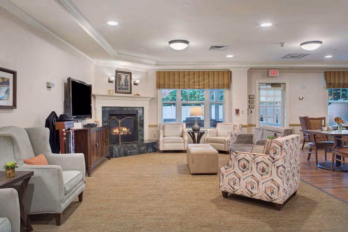 Spacious senior living common room with multiple armchairs, a fireplace, TV, and a dining area in the background.