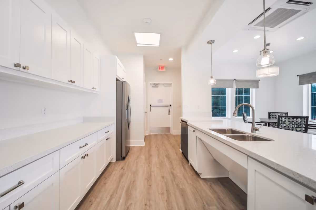 Bright modern kitchen with white cabinets, a large island with sink, stainless refrigerator, and pendant lights.