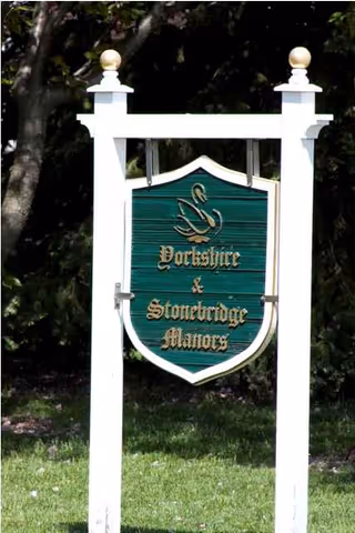 White wooden frame supports a green shield sign reading Yorkshire & Stonebridge Manors.