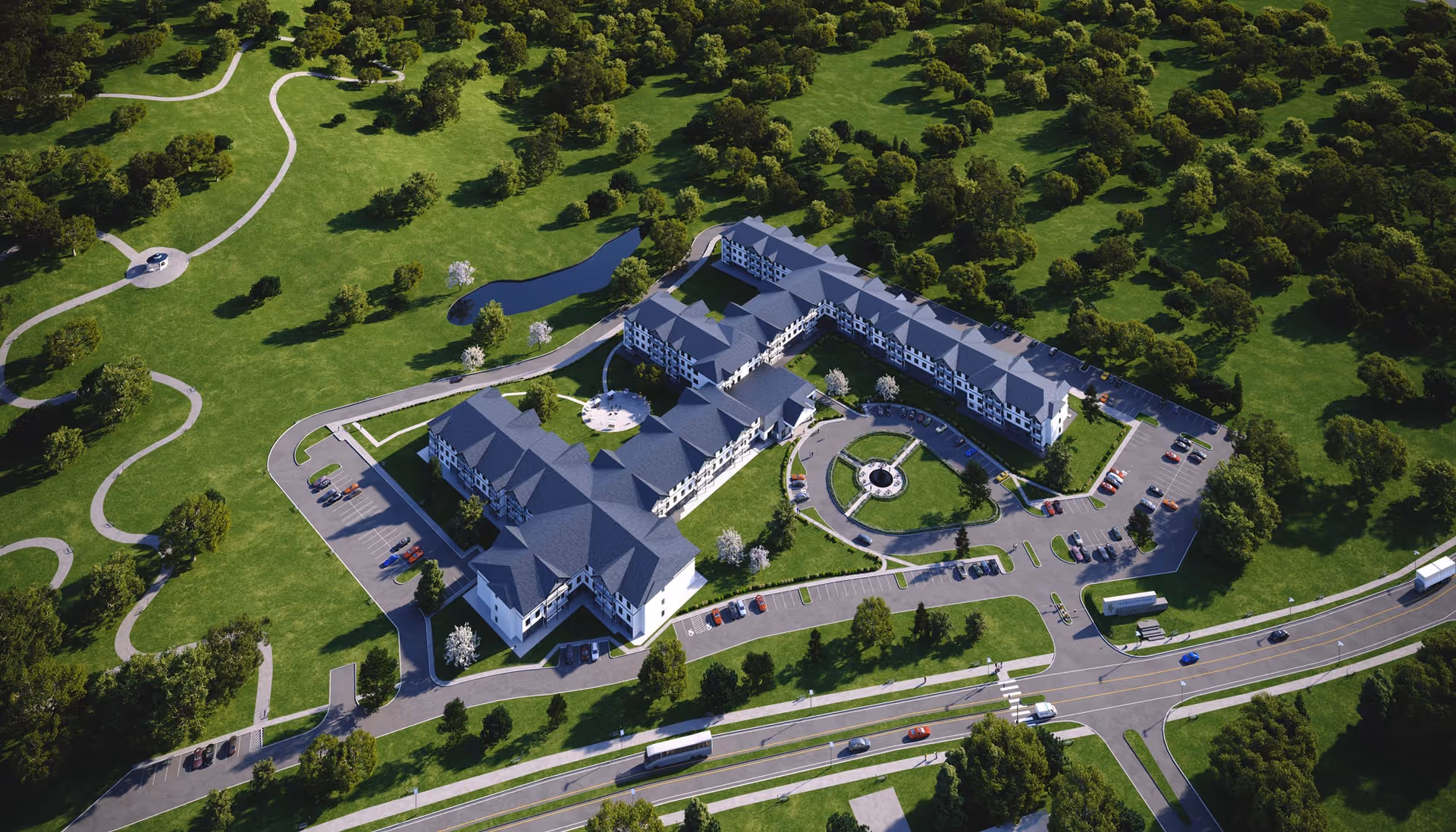 Aerial view of Hamilton Parc facility surrounded by green lawns, trees, walking paths, and parking lots. The building is large with multiple wings and a circular driveway at the front entrance. Roads and vehicles are visible near the facility.