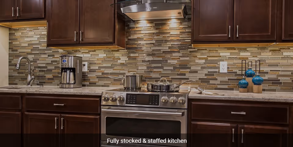 Modern kitchen with dark wood cabinets, a stainless steel stove with pots on the burners, a coffee maker on the counter, a sink with a faucet, and a decorative backsplash with under-cabinet lighting.