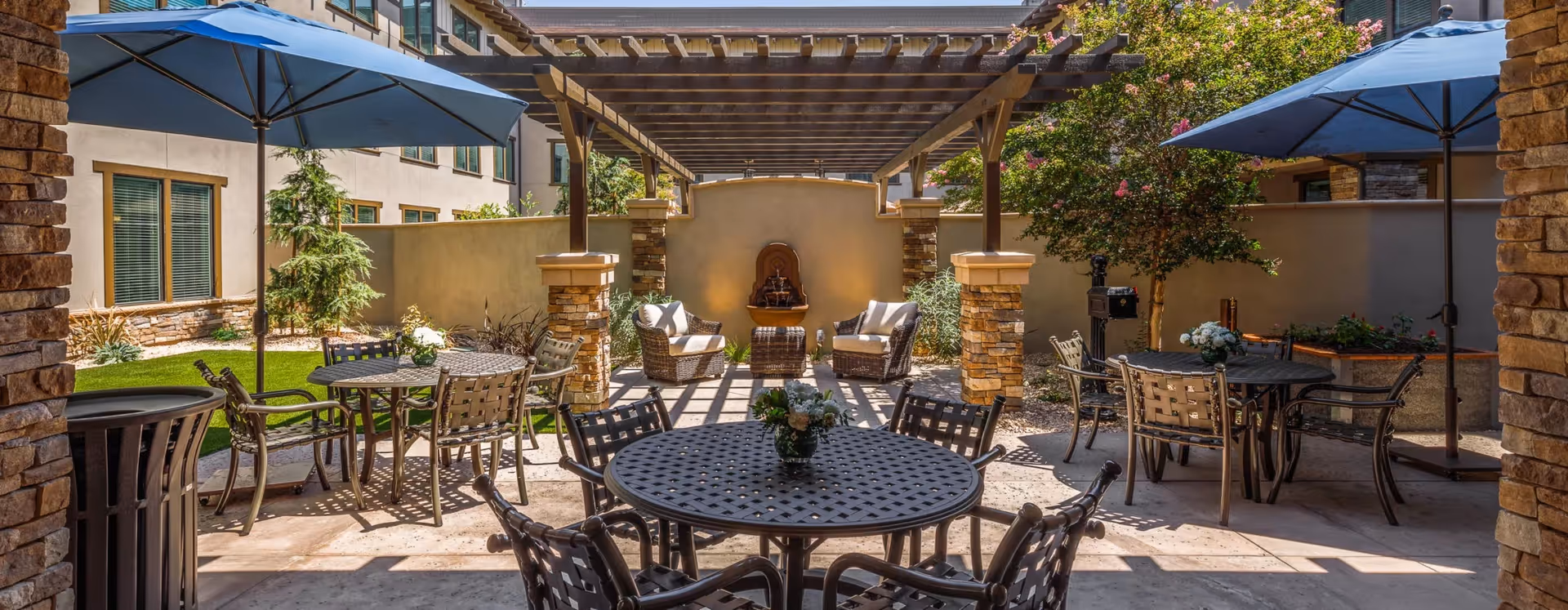 Outdoor courtyard patio with round metal tables, chairs, umbrellas, and a pergola with lounge seating.