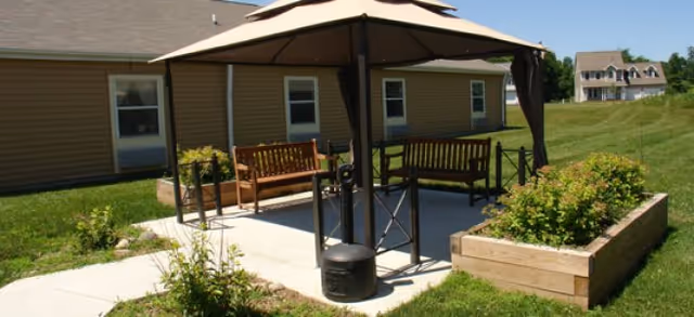 Outdoor patio with a canopy umbrella, wooden benches, raised planter boxes, and a building in the background.