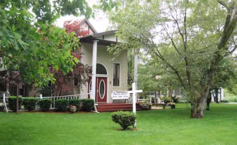 Exterior view of a house-style senior care home with a green lawn and trees.