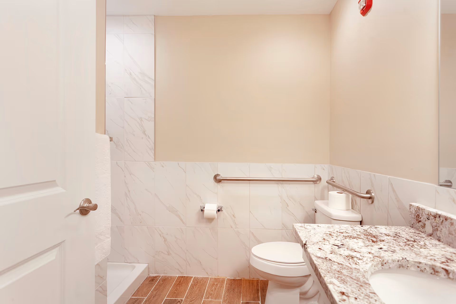 Bathroom with toilet, stainless grab bars, marble-tiled half wall, granite vanity with sink, and a walk-in shower.
