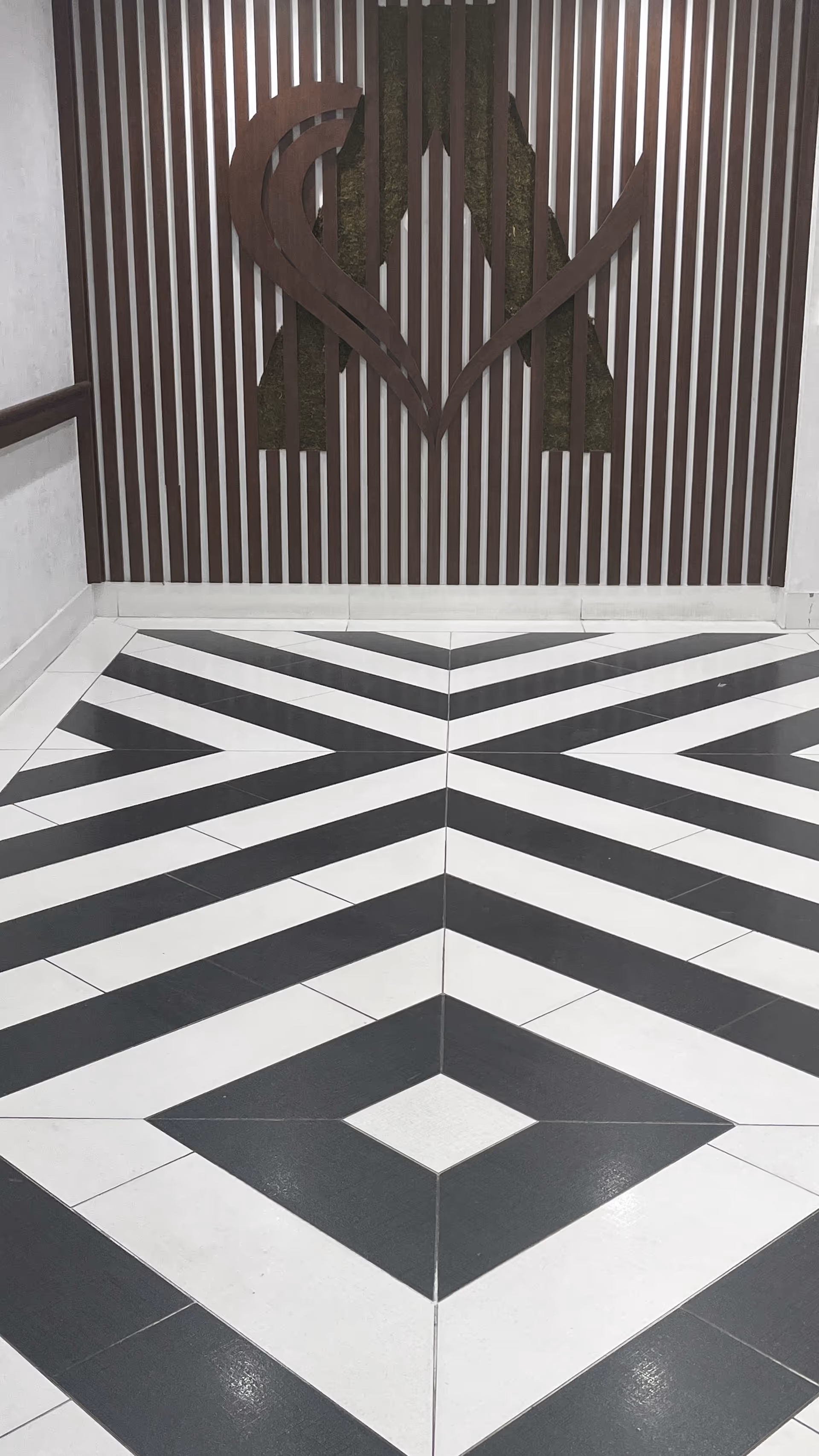 A hallway with a geometric black and white patterned floor and a wall featuring vertical wooden slats with a large decorative letter A in the center.