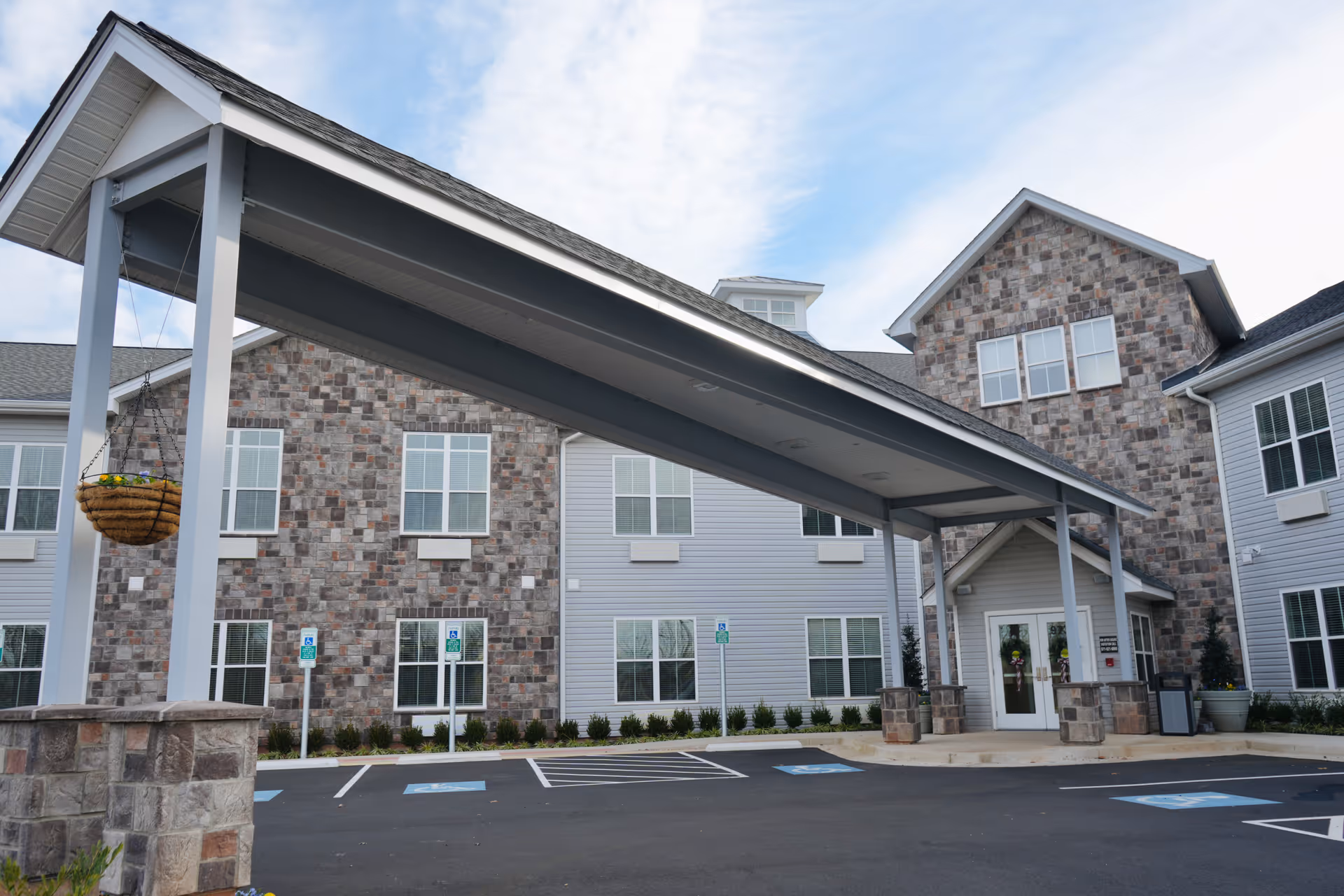 Exterior view of English Meadows Manassas Campus building with a covered entrance, stone and siding facade, multiple windows, and several handicap parking spaces in front.