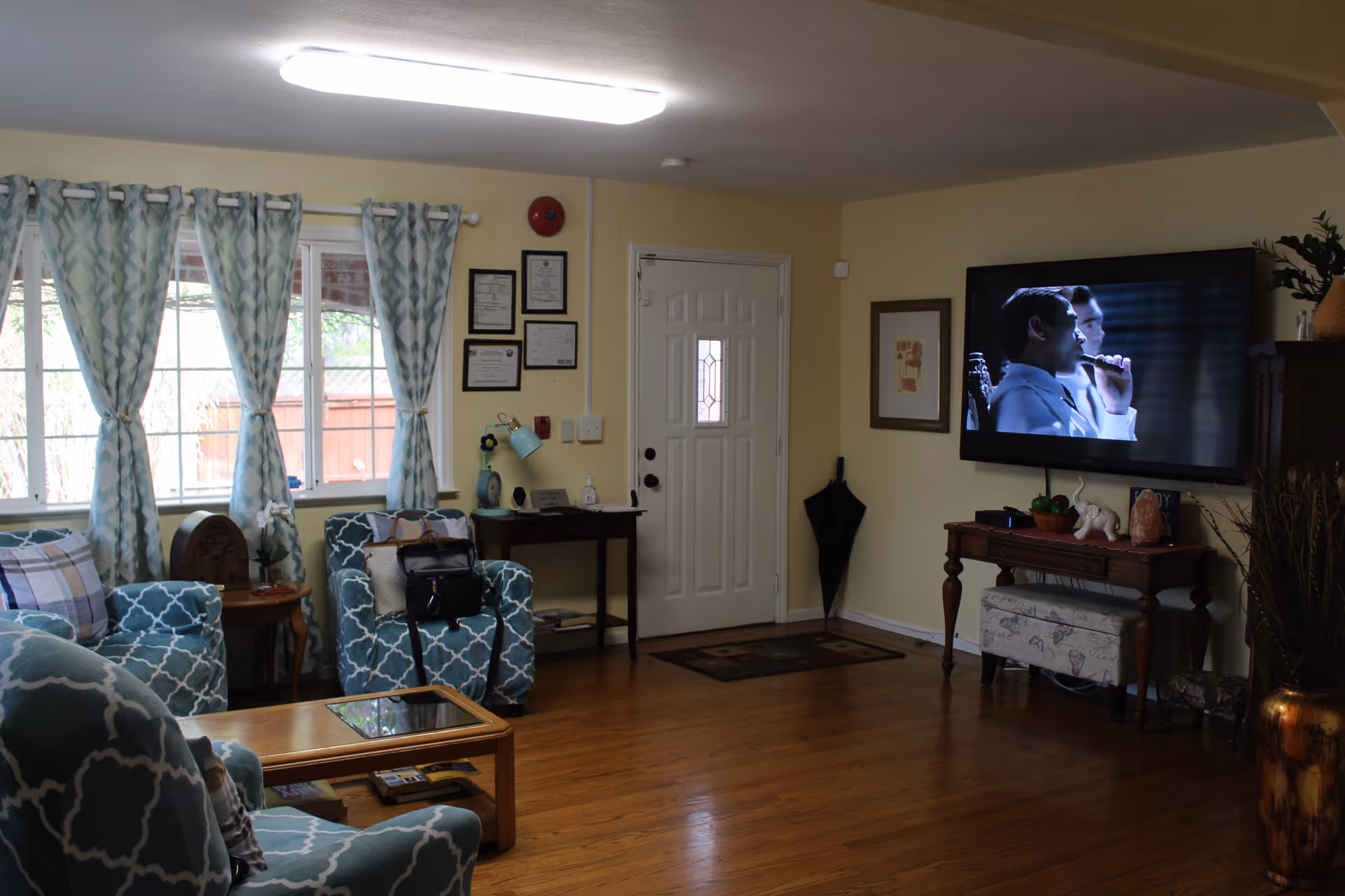 Cozy living room with patterned armchairs, a coffee table, wall-mounted TV and the front door visible.