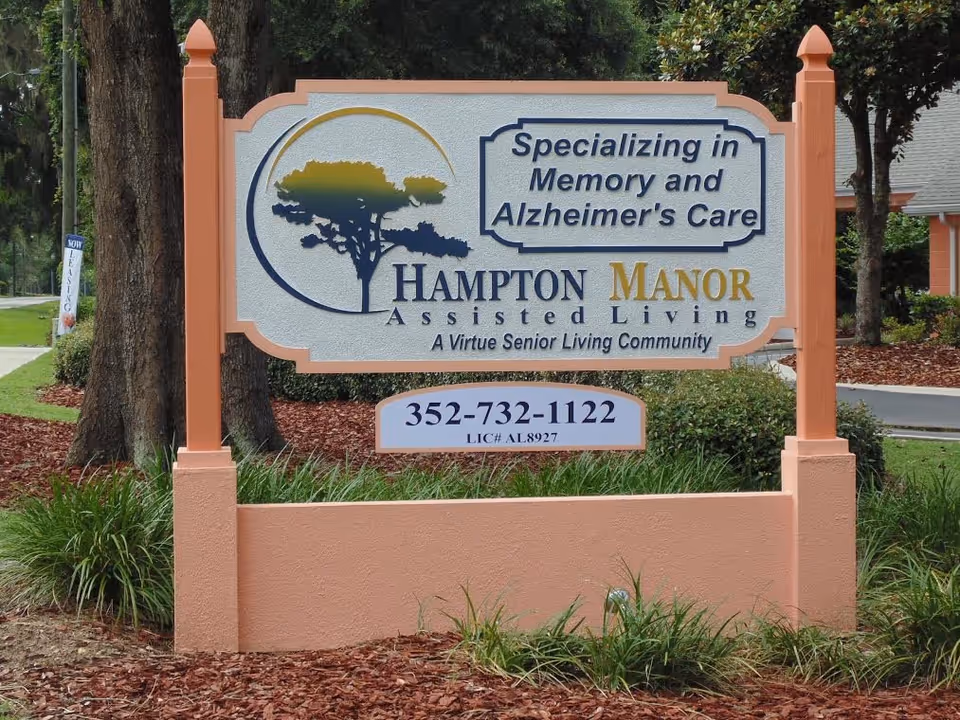 Prominent outdoor sign for Hampton Manor Assisted Living surrounded by mulch and greenery.