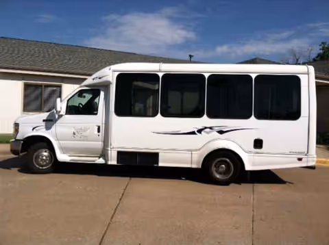 White shuttle bus parked beside a beige, single-story building.