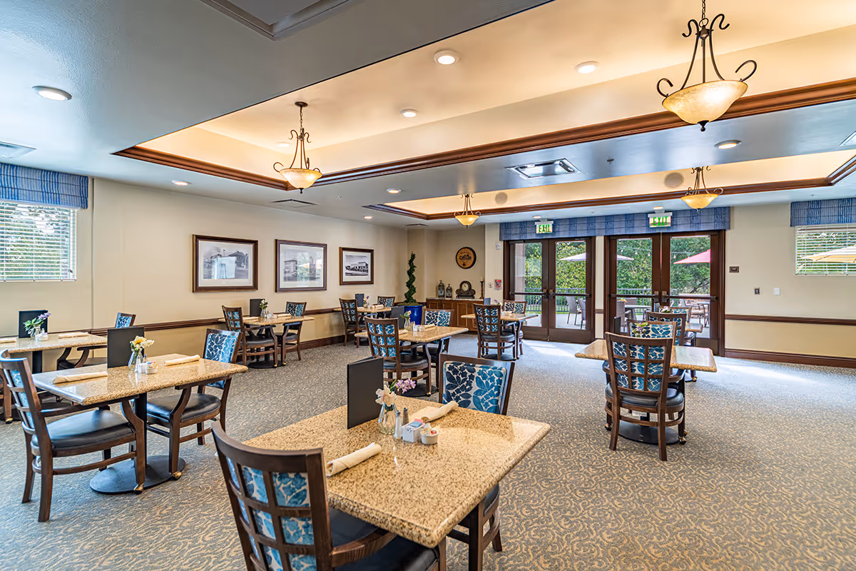 Bright, spacious dining room with multiple tables and chairs, decorative ceiling lights, and glass doors opening to an outdoor patio.