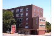 Exterior view of a brick senior living facility with a cross sign at entrance