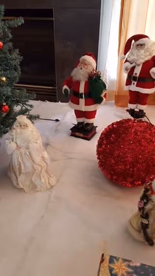 Christmas display in a living room featuring several Santa figurines, a large red glitter ball, and part of a decorated tree.