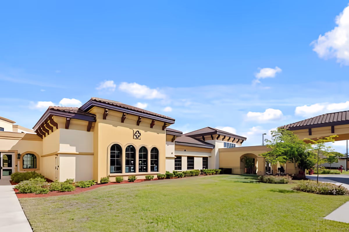 Exterior front view of a single-story Mediterranean-style building with arched windows, a covered entrance canopy, and a grassy lawn.