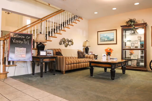 Comfortable lobby with a striped sofa, coffee table, display cabinet and a 'Welcome to Vintage Park' sign beneath a staircase.