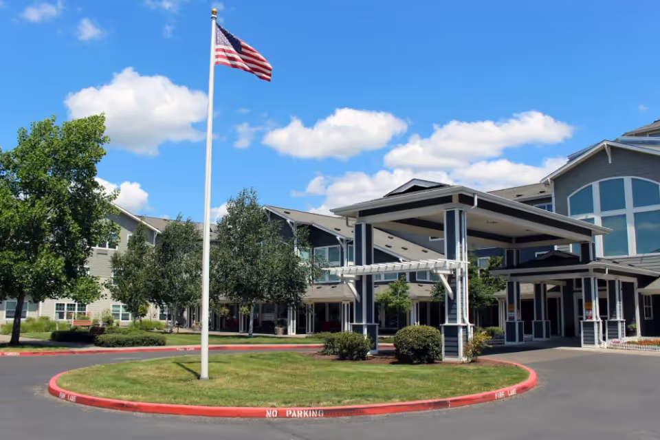 Front entrance of Timber Pointe Senior Living showing a flagpole in a circular driveway and a covered porte-cochère.