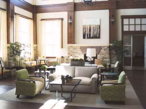 Bright senior living lobby with sofas, chairs, tables, and potted plants.