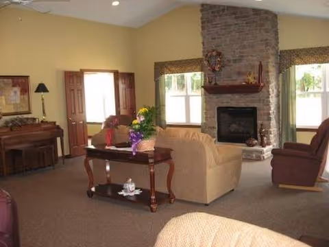 Cozy living room in a senior facility with fireplace, sofas, chairs, and flowers.