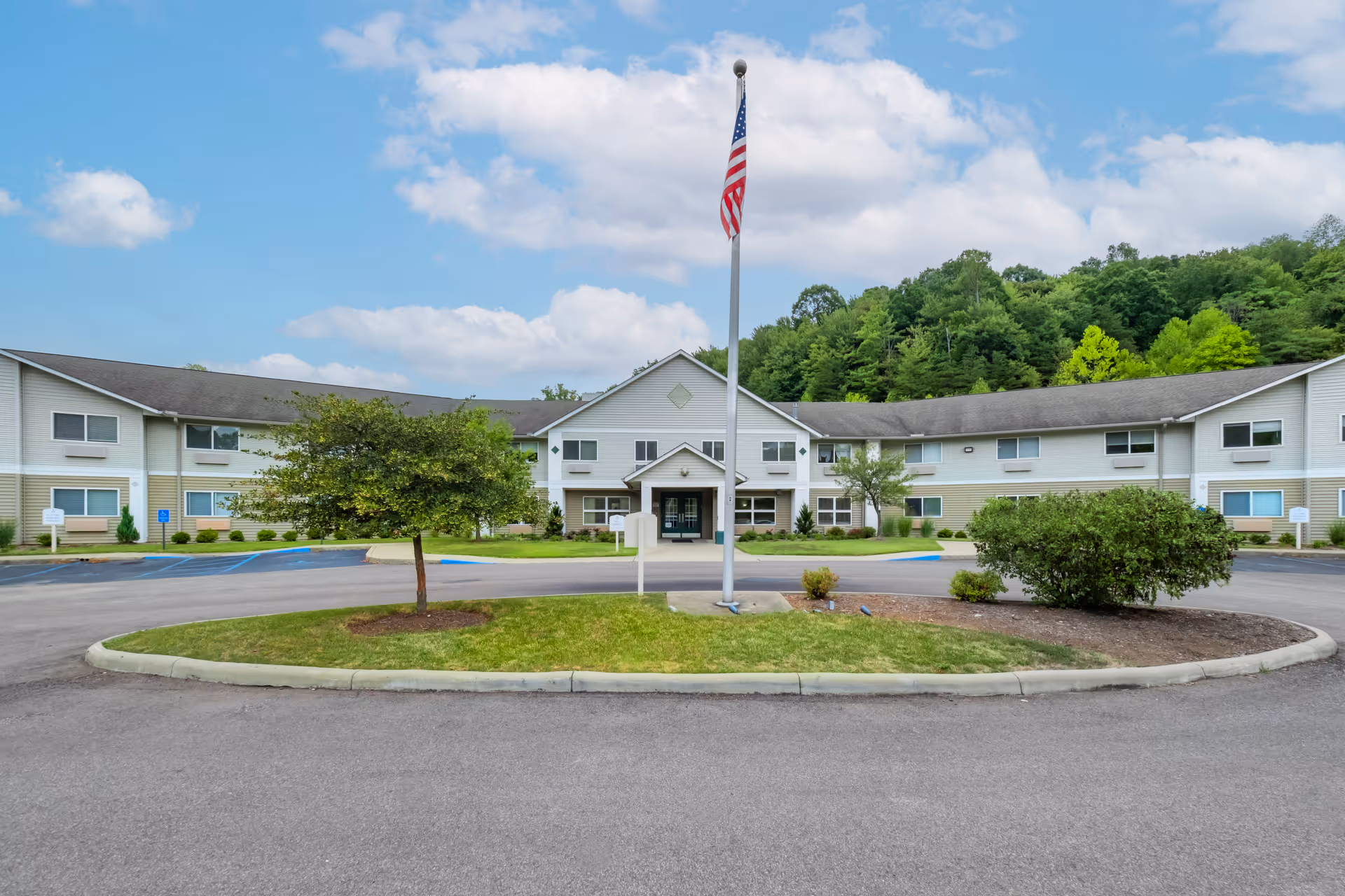 Front exterior of a two-story senior living building with a central entrance, flagpole, circular drive, and landscaping.