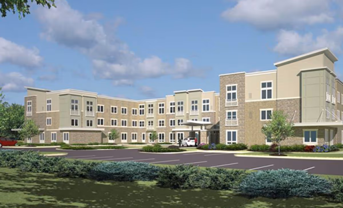 Front exterior of a three-story senior living facility with a covered entrance, parking lot, and landscaping under a partly cloudy sky.