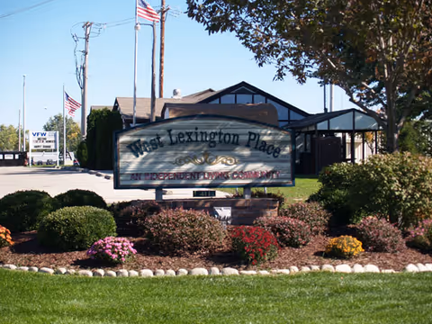 Landscaped front entrance with a sign reading "West Lexington Place, An Independent Living Community" and a single-story building behind it.