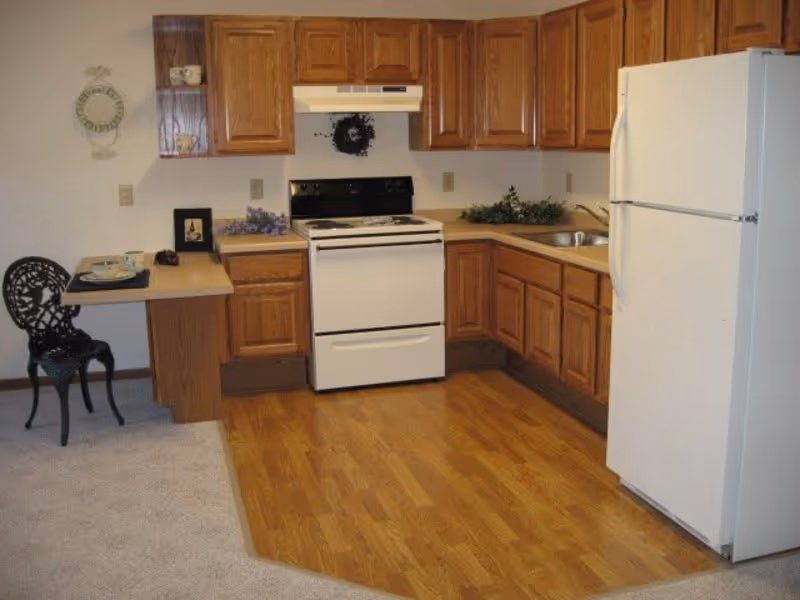 Small kitchen with wooden cabinets, a white stove and refrigerator, laminate flooring and a small dining nook.
