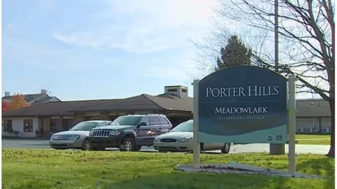 Front exterior of Meadowlark Retirement Village with a sign and parked cars.