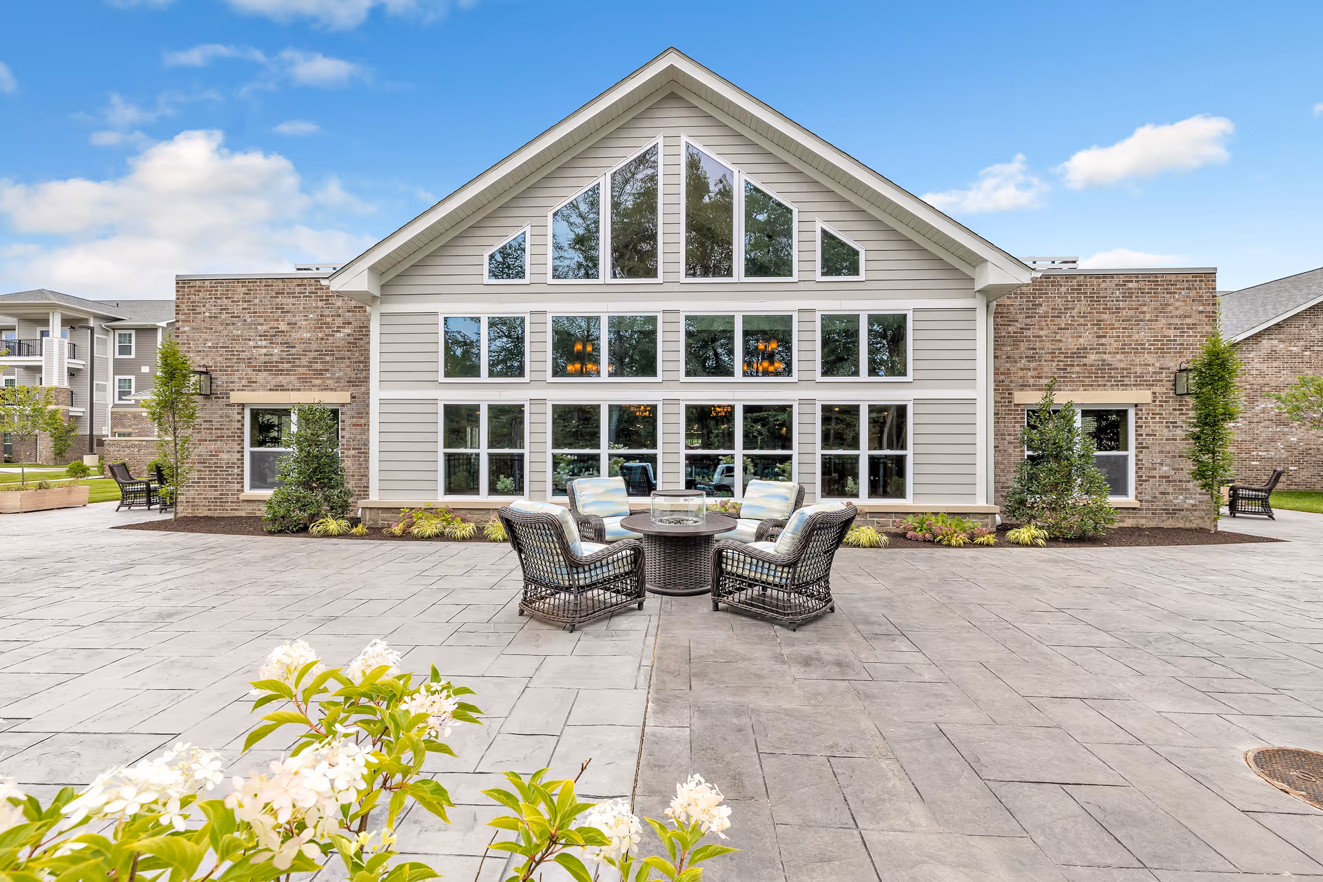 Front exterior of the River Valley Retirement Community building featuring large triangular windows, a paved courtyard, and wicker patio seating.