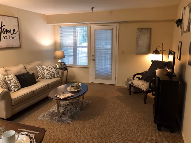 Cozy living room with a sofa, coffee table, armchair and TV stand facing a glass patio door with blinds.