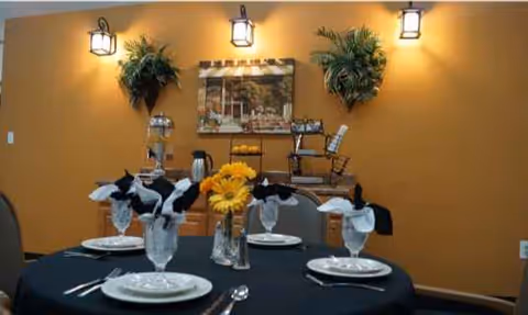 Round dining table set with plates, napkins, and sunflowers against an orange wall.