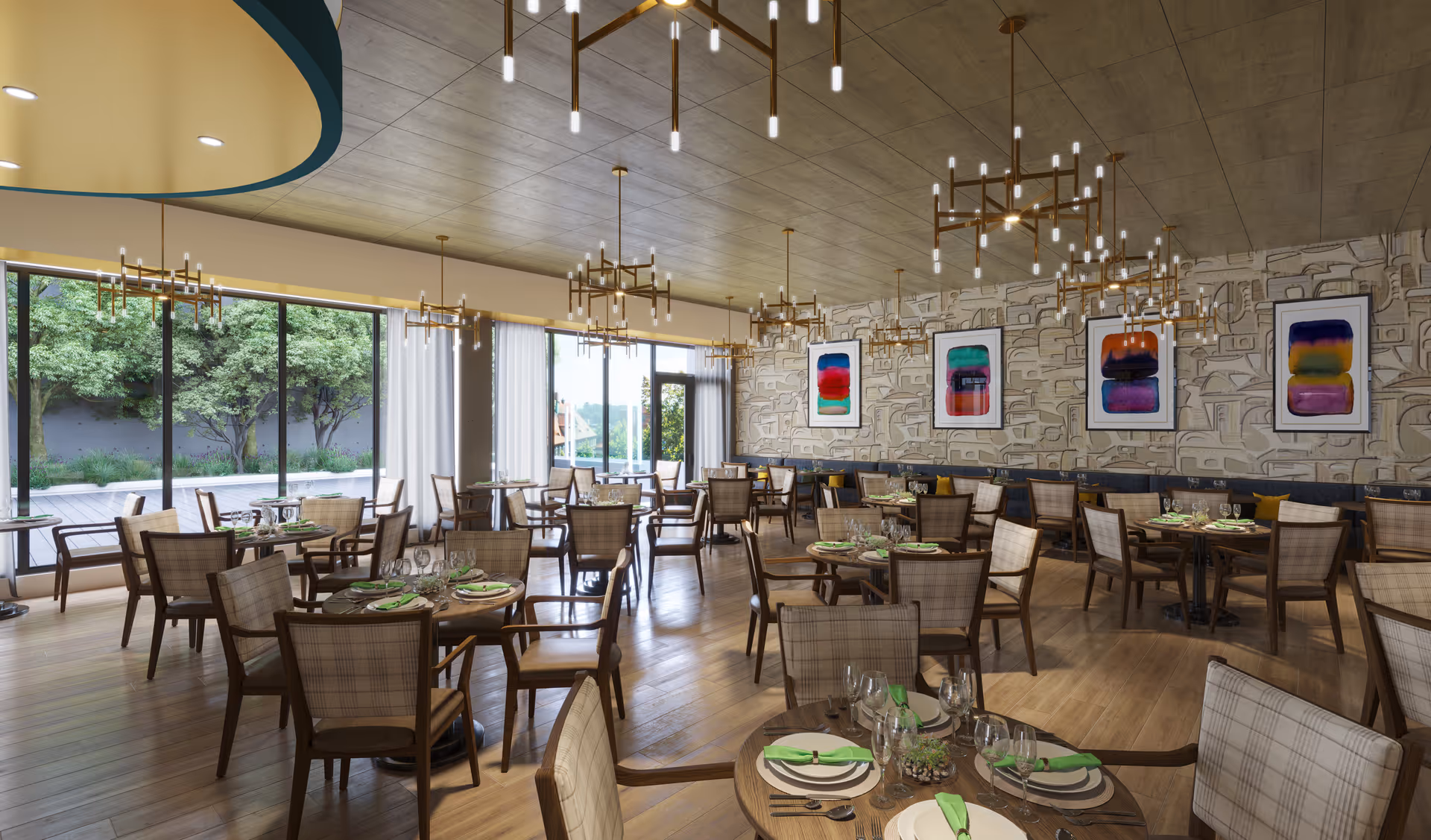 A spacious and well-lit dining room with multiple round wooden tables set with plates, glasses, and green napkins. The room features large floor-to-ceiling windows overlooking a garden with trees, modern chandeliers hanging from a wooden ceiling, and abstract colorful artwork on a textured wall.