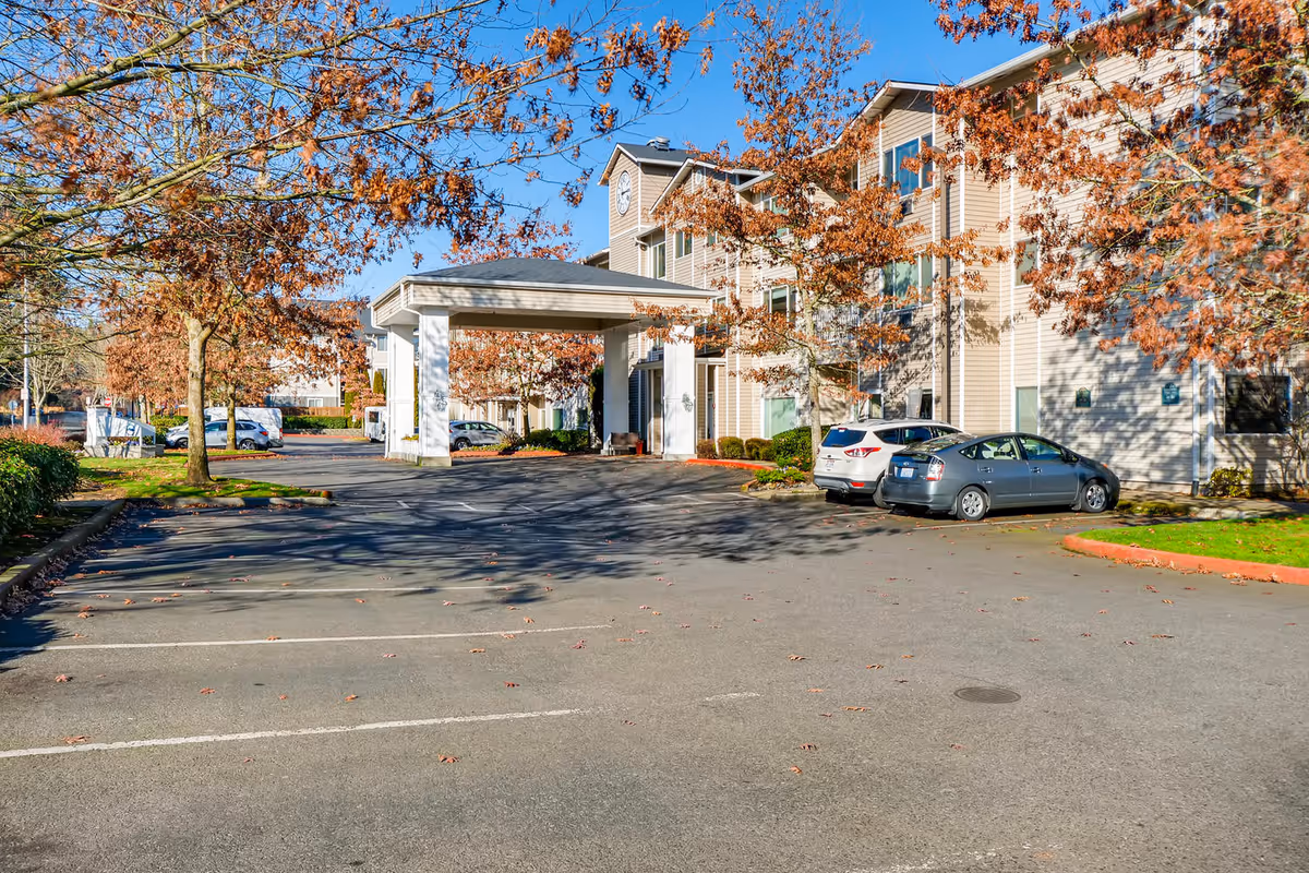 Exterior view of a senior living facility named Vancouver Pointe with a parking lot in front, several parked cars, and trees with autumn leaves under a clear blue sky.