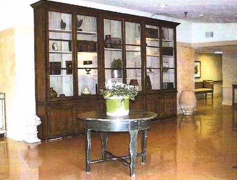 Large wooden display cabinet with glass doors, round plant table in a lobby.